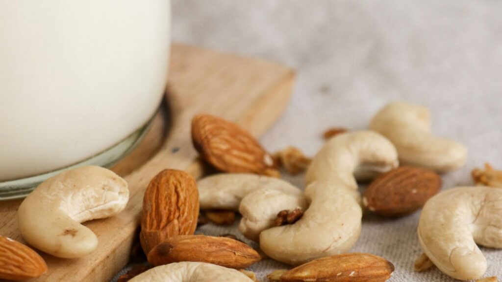 closeup of cashews and almonds next to glass of plant milk