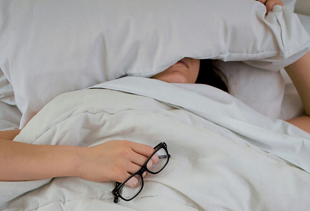 woman lying in bed sick with pillow over face