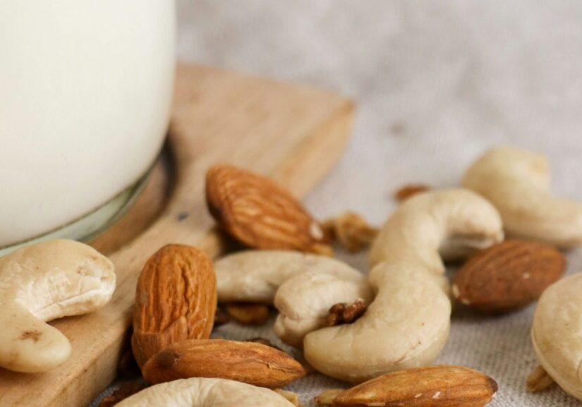 closeup of cashews and almonds next to glass of plant milk