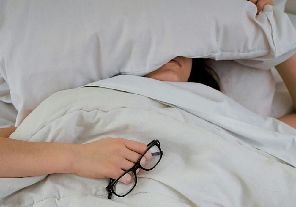 woman lying in bed sick with pillow over face